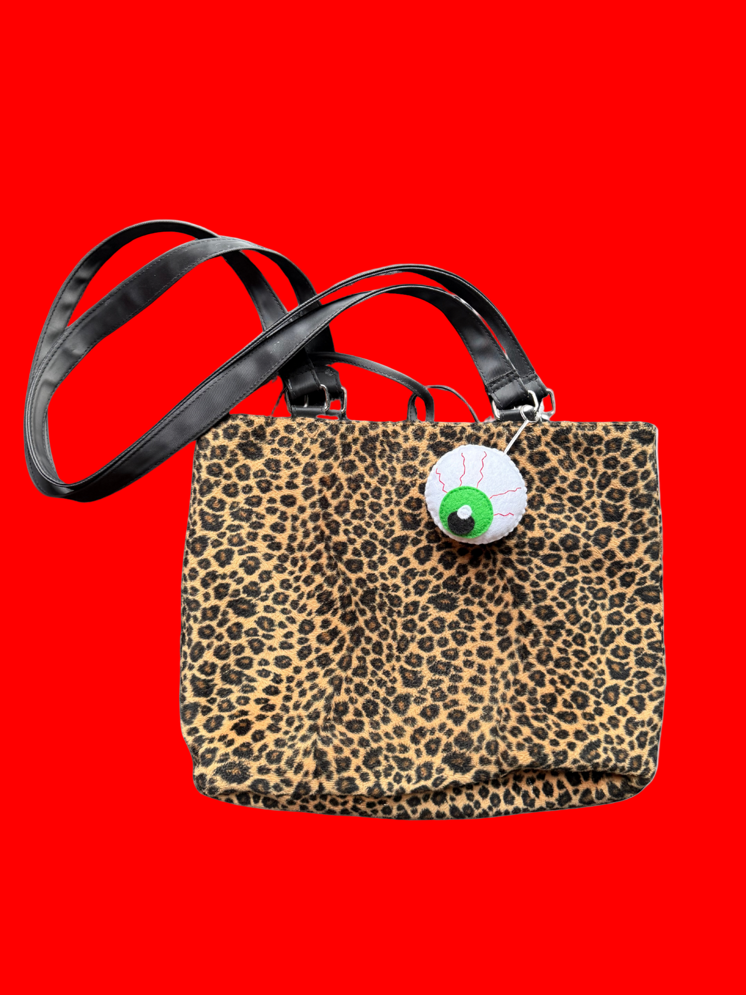 Leopard print handbag with a green and white eye charm on a white background