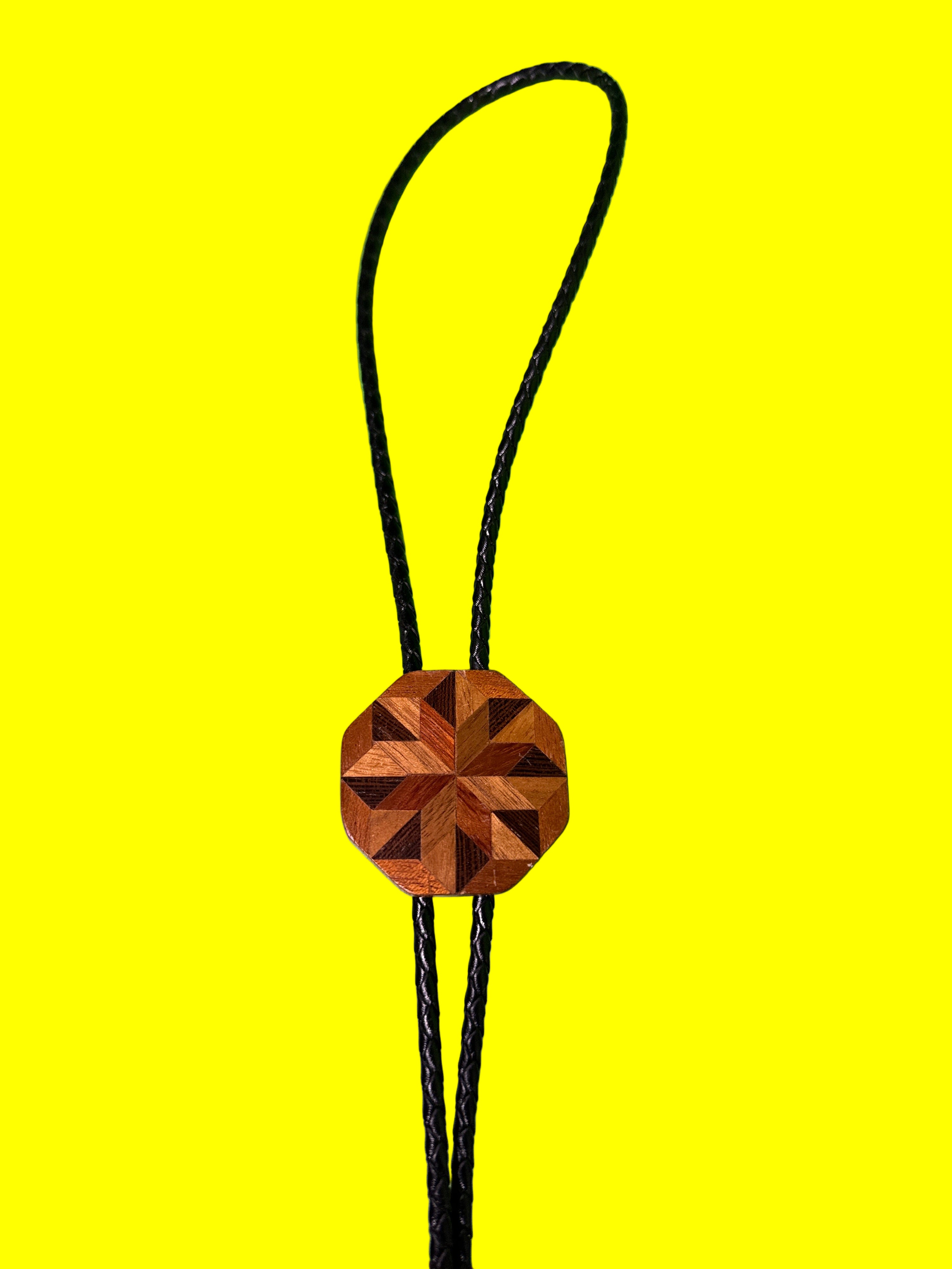 Wooden geometric pendant on a black cord against a yellow background