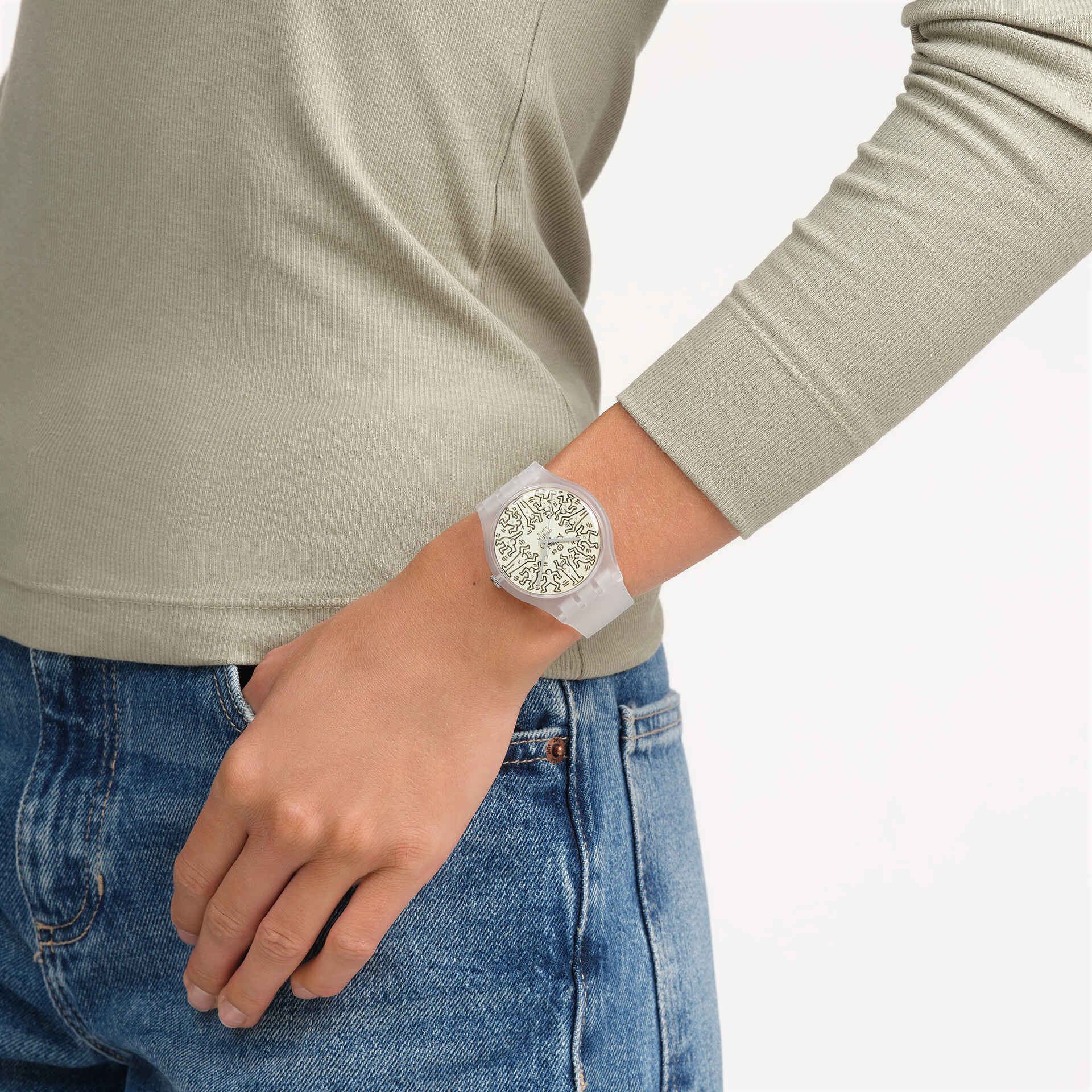 Person wearing a light gray long-sleeve shirt and blue jeans with a decorative watch on a white background